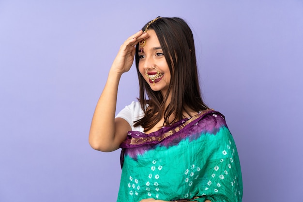 Junge indische Frau lokalisiert auf lila Wand, die mit Hand mit glücklichem Ausdruck salutiert