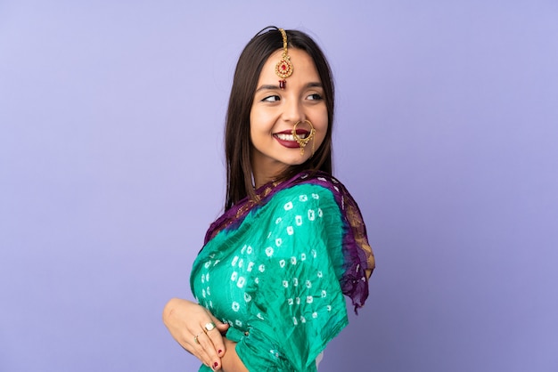 Junge indische Frau lokalisiert auf lila Wand mit verschränkten Armen und glücklich