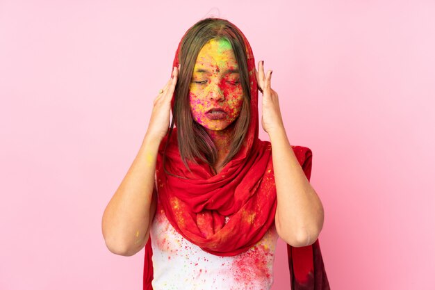 Junge indische Frau mit bunten Holi-Pulvern auf ihrem Gesicht auf rosa Wand mit Kopfschmerzen