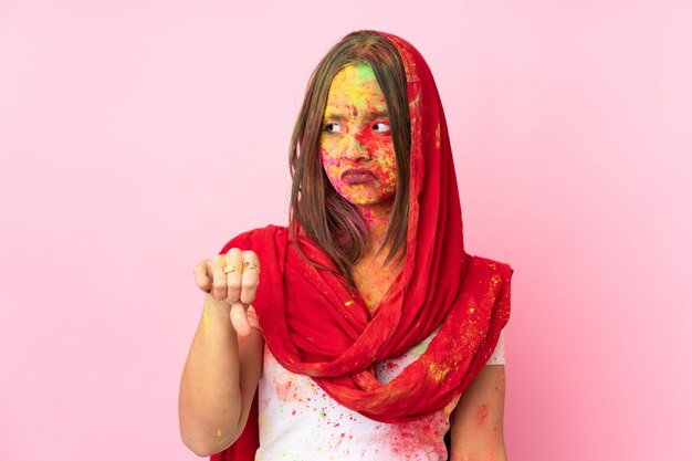 Junge indische Frau mit bunten Holi-Pulvern auf ihrem Gesicht lokalisiert auf rosa Wand, die Daumen unten mit negativem Ausdruck zeigt