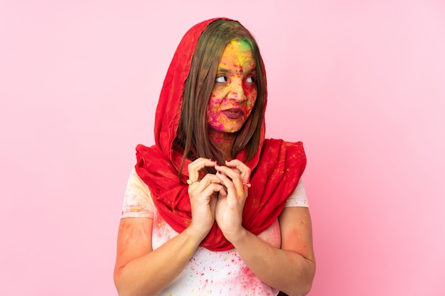 Junge indische Frau mit bunten Holi-Pulvern auf ihrem Gesicht lokalisiert auf rosa Wand, die etwas entwirft