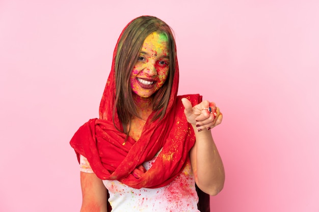 Junge indische Frau mit bunten Holipulvern auf ihrem Gesicht auf rosa Wand, die eine Daumen hoch Geste gibt