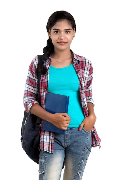Junge indische Frau mit Rucksack stehend und hält Notizbücher, posierend auf einer weißen Wand.