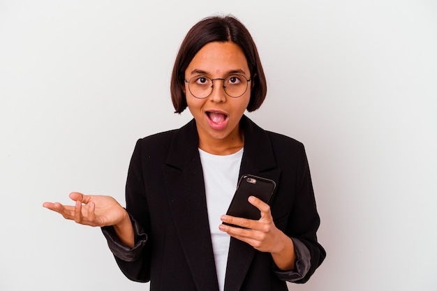 Junge indische Geschäftsfrau, die ein Telefon isoliert, überrascht und schockiert hält.