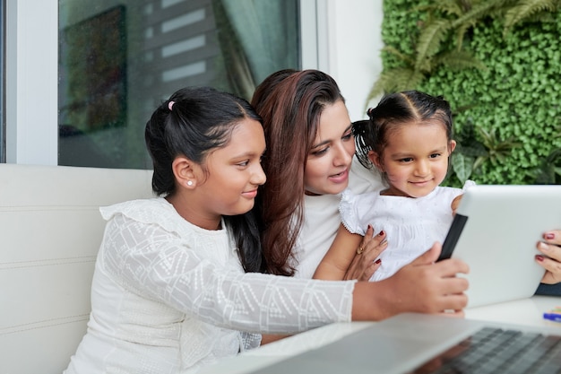 Junge indische Mutter und ihre beiden Töchter schauen sich Cartoons oder Lehrvideos auf einem Tablet-Computer an