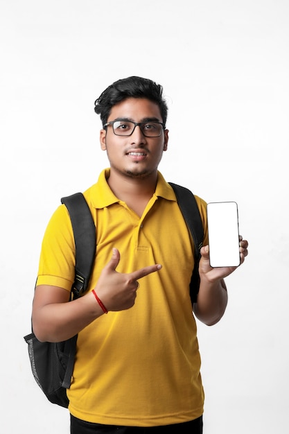 Junge indische Studentin, die Handy auf weißem Hintergrund zeigt.
