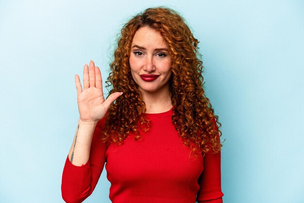 Junge Ingwer-kaukasische Frau isoliert auf blauem Hintergrund, die fröhlich lächelt und die Nummer fünf mit den Fingern zeigt