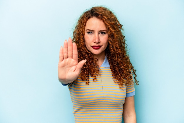Junge Ingwer-kaukasische Frau isoliert auf blauem Hintergrund, die mit ausgestreckter Hand steht und ein Stoppschild zeigt, das Sie verhindert