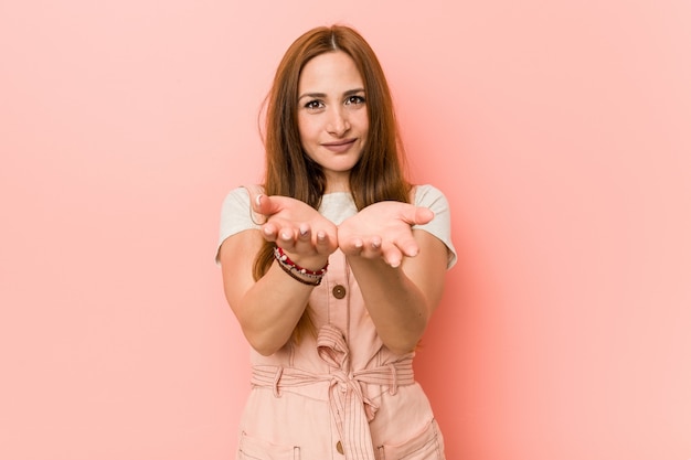 Junge Ingwerfrau mit den Sommersprossen, die etwas mit den Palmen, Kamera anbietend halten.