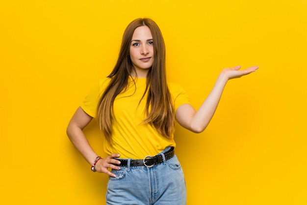 Junge IngwerRothaarigefrau, die einen Kopienraum auf einer Palme zeigt und eine andere Hand auf Taille hält.