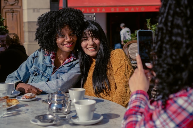 Junge interrassische Freundinnen latina und haitianische trinken Kaffee an einem Herbstnachmittag im Freien machen ein Foto mit einem Handy