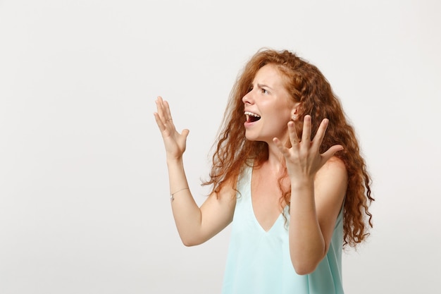 Junge irritierte verwirrte rothaarigefrau in der beiläufigen hellen kleidung, die lokalisiert auf weißem wandhintergrund aufwirft. menschen aufrichtige emotionen lifestyle-konzept. kopieren sie platz. beiseite schauen, hände ausbreiten.