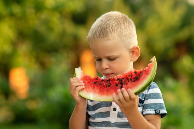 Junge isst Wassermelone im Freien. Sommerurlaub auf dem Land.