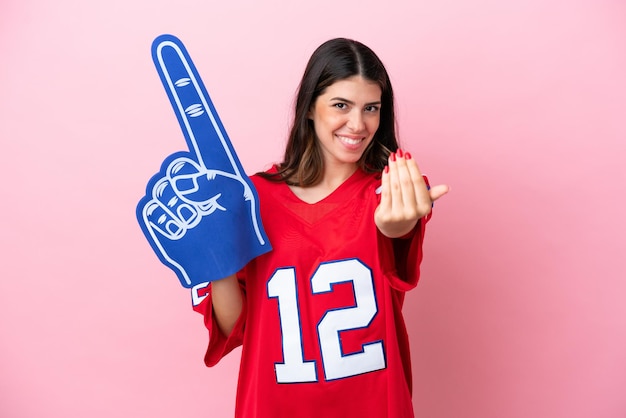 Junge italienische Fanfrau mit Schaumhand isoliert auf rosa Hintergrund, die einlädt, mit der Hand zu kommen Glücklich, dass du gekommen bist