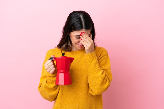 Junge italienische Frau, die eine Kaffeemaschine isoliert auf rosa Hintergrund mit müdem und krankem Ausdruck hält