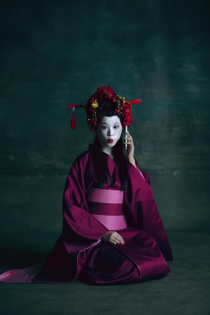 Junge japanische Frau als Geisha auf dunkelgrünem. Retro-Stil, Vergleich des Epochenkonzepts.