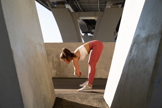 Junge Joggerin bereiten sich auf die Laufarbeit vor, die Beine im Freien unter einer Brücke ausdehnt