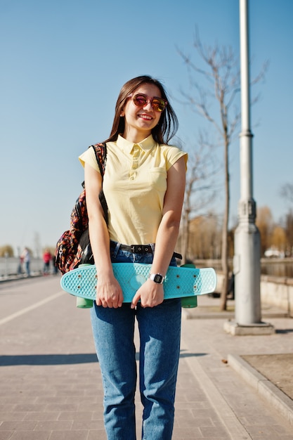 Junge Jugendliche mit kleinem Skateboard, Penny Board, Abnutzung auf gelbem T-Shirt, Jeans und Sonnenbrille.