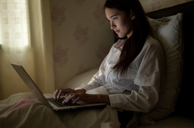 Junge junge schöne Frau liegt im Bett in der Nacht und arbeitet an ihrem Laptop Frau liegt im Bett