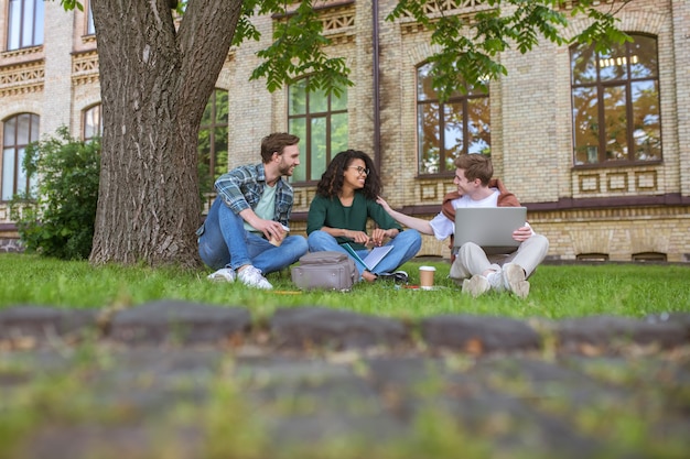 Junge Jungs und ein Mädchen sitzen auf dem Gras in der Nähe des College-Gebäudes
