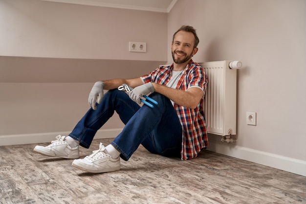 Junge kaukasische Arbeiter sitzen auf dem Boden mit Schraubenschlüssel in der Hand