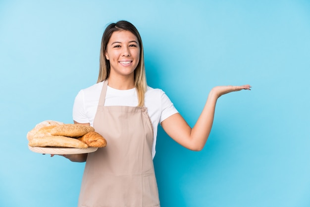 Junge kaukasische bäckerfrau lokalisiert, einen kopienraum auf einer palme zeigend und eine andere hand auf taille halten.