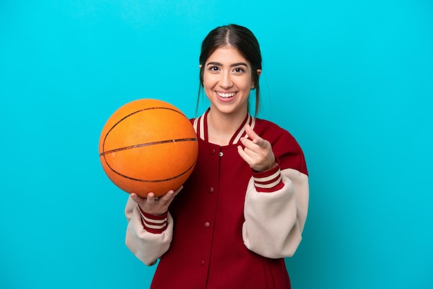 Junge kaukasische Basketballspielerfrau isoliert auf blauem Hintergrund überrascht und zeigt nach vorne