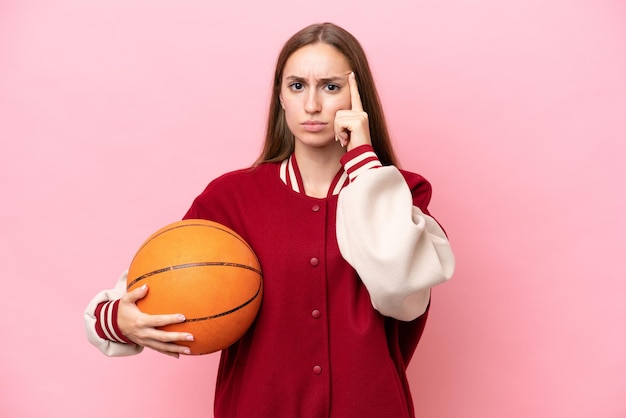 Junge kaukasische Basketballspielerin über isoliert auf rosafarbenem Hintergrund, die eine Idee denkt