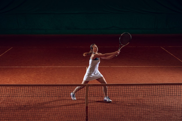 Junge kaukasische Berufssportlerin, die Tennis auf Sportplatzwand spielt.