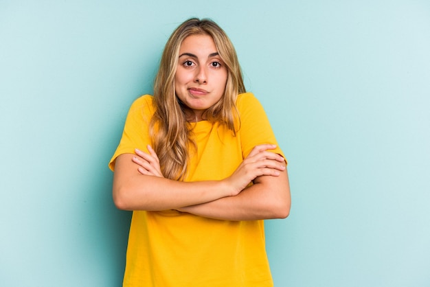 Junge kaukasische blonde Frau, die auf blauem Hintergrund isoliert ist, zuckt mit den Schultern und öffnet die Augen verwirrt.