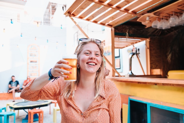 Junge kaukasische blonde Frau glücklich für eine Feier und ein Glas Bier trinkend