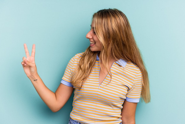 Junge kaukasische blonde Frau isoliert auf blauem Hintergrund fröhlich und sorglos, die ein Friedenssymbol mit den Fingern zeigt.