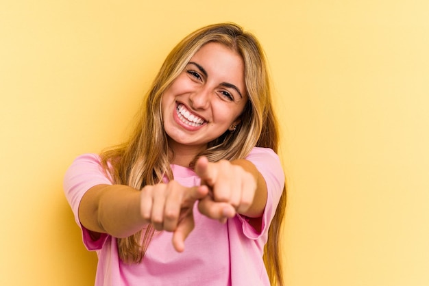 Junge kaukasische blonde Frau isoliert auf gelbem Hintergrund, die mit den Fingern auf die Vorderseite zeigt.