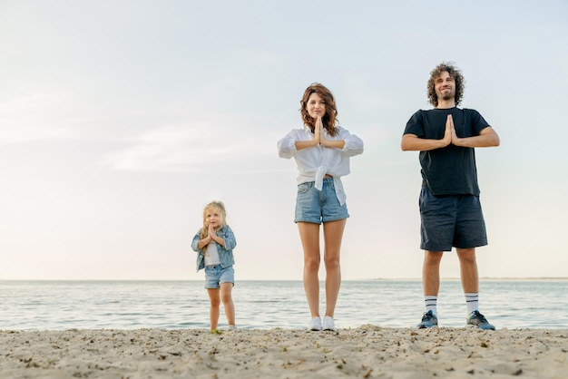 Junge kaukasische Familie, die zusammen meditiert, während sie Yoga am Strand macht