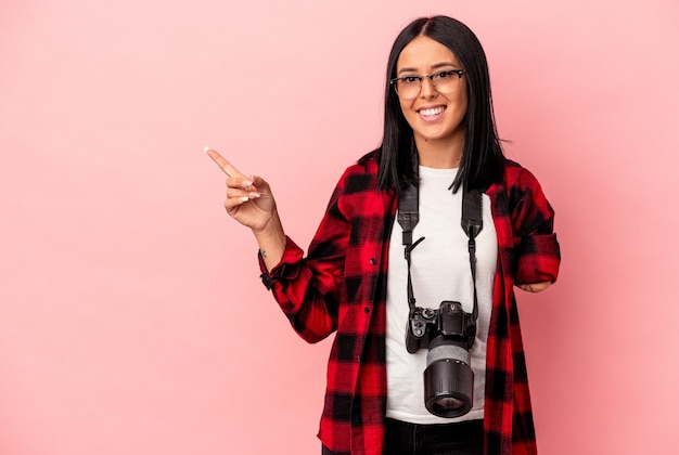 Junge kaukasische Fotografiefrau mit einem Arm einzeln auf rosafarbenem Hintergrund lächelnd und zur Seite zeigend, etwas an der Leerstelle zeigend.