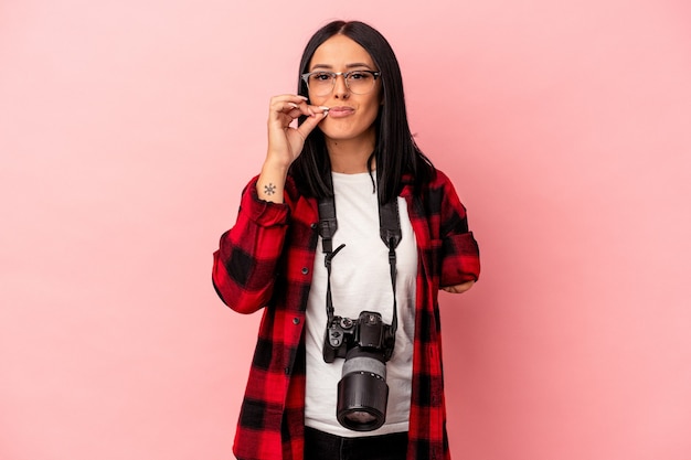 Junge kaukasische Fotografiefrau mit einem Arm lokalisiert auf rosa Hintergrund mit Fingern auf den Lippen, die ein Geheimnis halten.