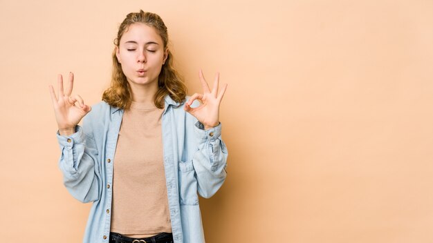 Junge kaukasische Frau auf beige Wand entspannt sich nach hartem Arbeitstag, der Yoga durchführt.