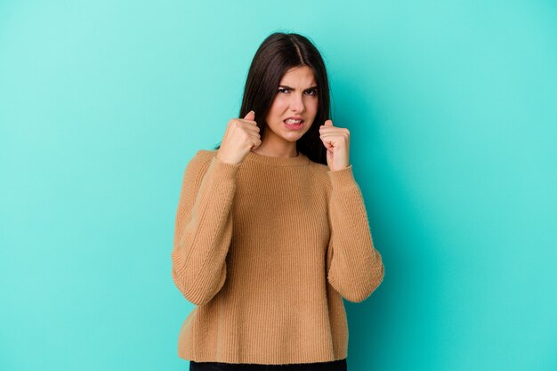 Junge kaukasische Frau auf blauem Aufruhr, der mit angespannten Händen schreit.