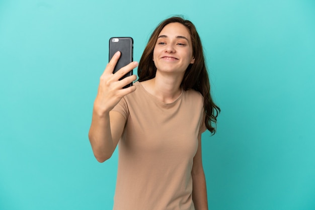 Junge kaukasische Frau auf blauem Hintergrund isoliert, die ein Selfie mit dem Handy macht