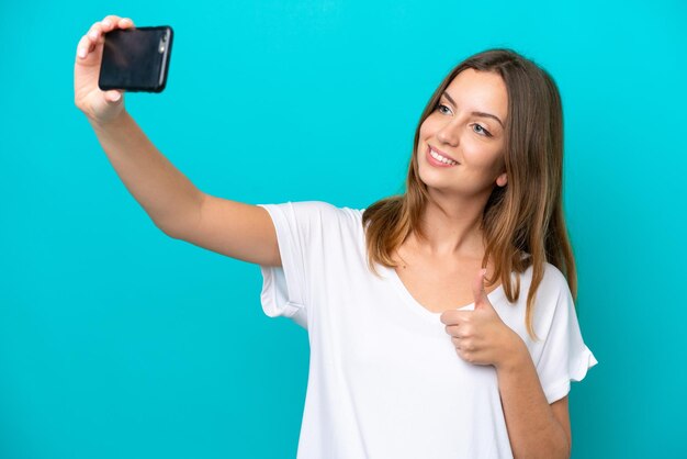 Junge kaukasische Frau auf blauem Hintergrund isoliert, die ein Selfie mit dem Handy macht