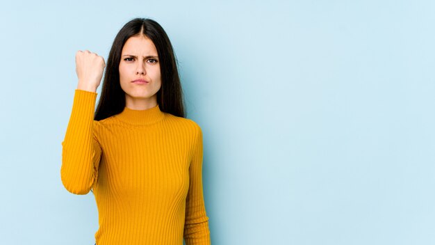 Junge kaukasische frau auf blauer wand, die mit einem aggressiven gesichtsausdruck zeigt.