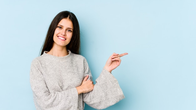 Junge kaukasische Frau auf der blauen Wand lächelnd, die mit Zeigefinger weg zeigt.