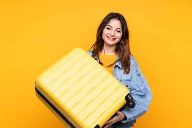 Junge kaukasische Frau auf gelber Wand im Urlaub mit Reisekoffer