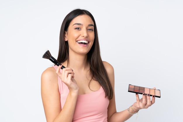 Junge kaukasische Frau auf weißer Wand mit Make-up-Palette und glücklich