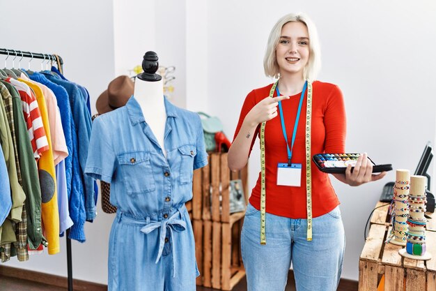 Junge kaukasische Frau, die als Designerin in einer Boutique arbeitet, lächelt glücklich und zeigt mit Hand und Finger