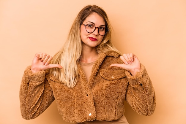 Junge kaukasische Frau, die auf beigem Hintergrund isoliert ist, fühlt sich stolz und selbstbewusst, um dem Beispiel zu folgen