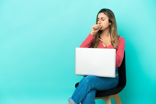 Junge kaukasische Frau, die auf einem Stuhl sitzt, mit ihrem PC auf blauem Hintergrund isoliert, leidet an Husten und fühlt sich schlecht