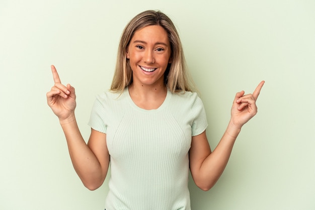 Junge kaukasische Frau, die auf grünem Hintergrund isoliert ist, zeigt an, dass beide Vorderfinger eine Leerstelle zeigen.