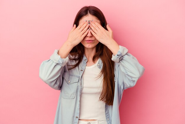 Junge kaukasische Frau, die auf rosafarbenem Hintergrund isoliert ist, hat Angst, die Augen mit den Händen zu bedecken.