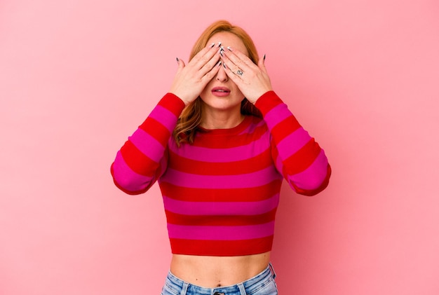 Junge kaukasische Frau, die auf rosafarbenem Hintergrund isoliert ist, hat Angst, die Augen mit den Händen zu bedecken.